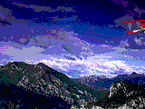 Old red bi-plane flies by in front of mountains